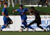 Sicheren Sieg verspielt: Ibach teilt die Punkte mit Malcantone Two soccer players in blue and black jerseys challenge for the ball along advertising boards on a grassy field.