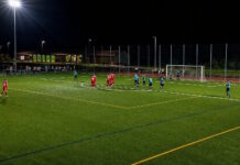 Niederlage gegen Sarnen: Engelberg mit frühem Out im Cup Nighttime soccer match: red team huddles near the center while teal opponents stand nearby under bright floodlights in a fenced stadium area.