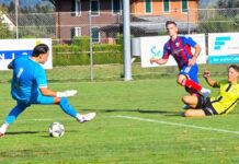 Brunnen siegt zum Saisonauftakt in Eschenbach Soccer scene: blue-clad goalkeeper about to kick a ball as a yellow-shirted opponent slides in from the right on a green field.