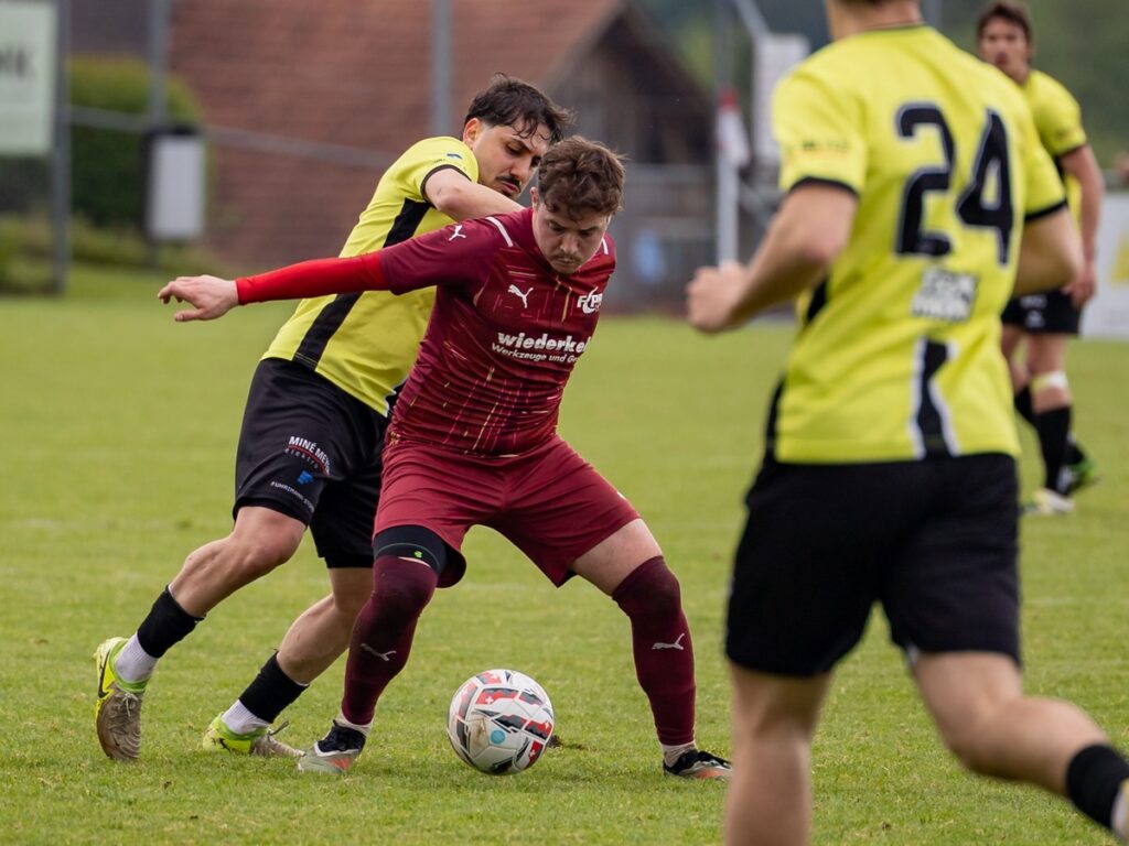 fceschenbach_fcperlenbuchrain2-1024x768 Maroon-clad player shields and dribbles the ball as a yellow-clad defender closes in on a grassy field