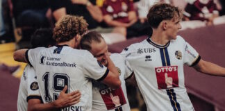Soccer players in white jerseys embrace in celebration on the field.