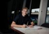 FC Luzern verpflichtet Daniel Mikolajewski leihweise Young man with curly hair signs documents at a marble table in a bright, modern room with large windows behind him.
