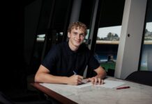 FC Luzern verpflichtet Daniel Mikolajewski leihweise Young man with curly hair signs documents at a marble table in a bright, modern room with large windows behind him.