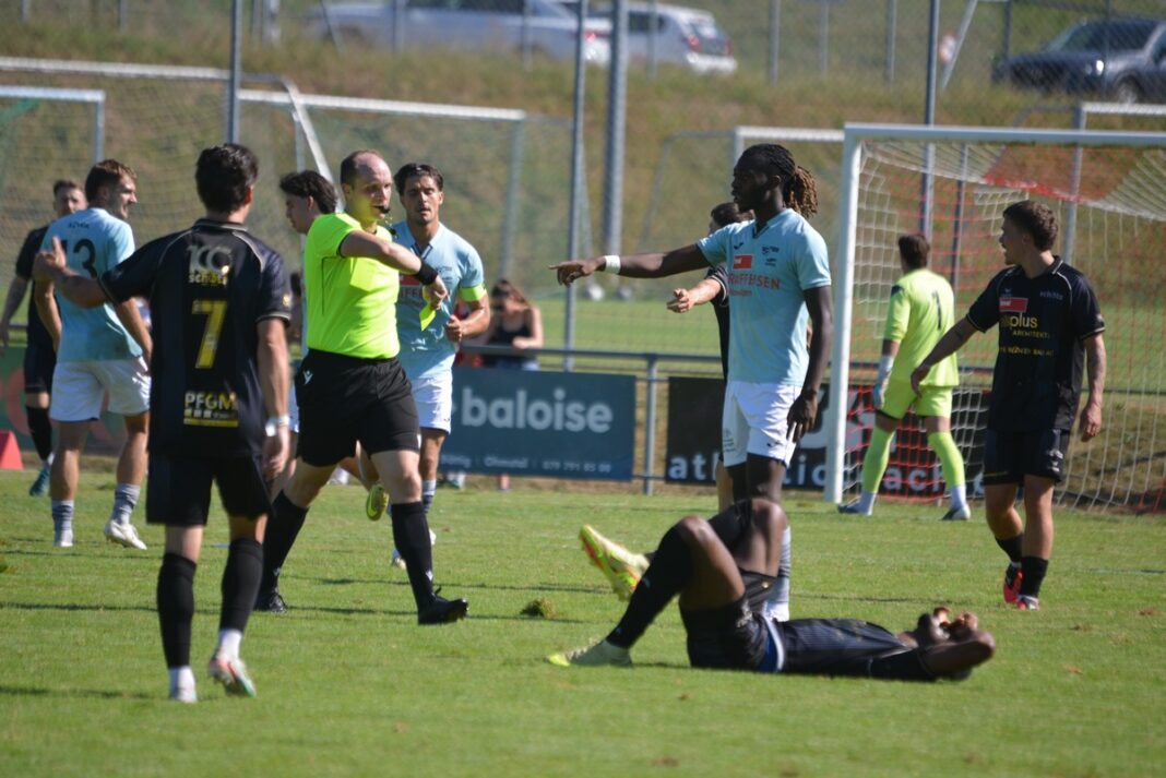 fcschoetz_scbuochs25 Soccer match scene with a player on the ground as others stand around and a referee points a call toward the field.
