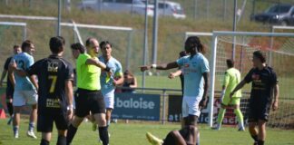 Soccer match scene with a player on the ground as others stand around and a referee points a call toward the field.
