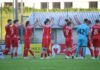 Schattdorf unterliegt Aufsteiger Stans knapp mit 1:2 Soccer teammates in red jerseys high-fiving along the sideline after a play, with a blue-clad goalkeeper nearby on a green field.