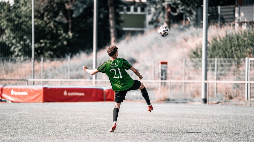 luzernersc_rf1 Soccer player in a green jersey with number 21 kicks a ball in an outdoor field.