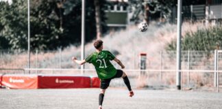 Soccer player in a green jersey with number 21 kicks a ball in an outdoor field.