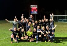 12 Tore: Souveräner Saisonauftakt für die TRE Frauen Group of female soccer players in dark uniforms celebrate on a lit grass field, one player lifted on teammates' shoulders.